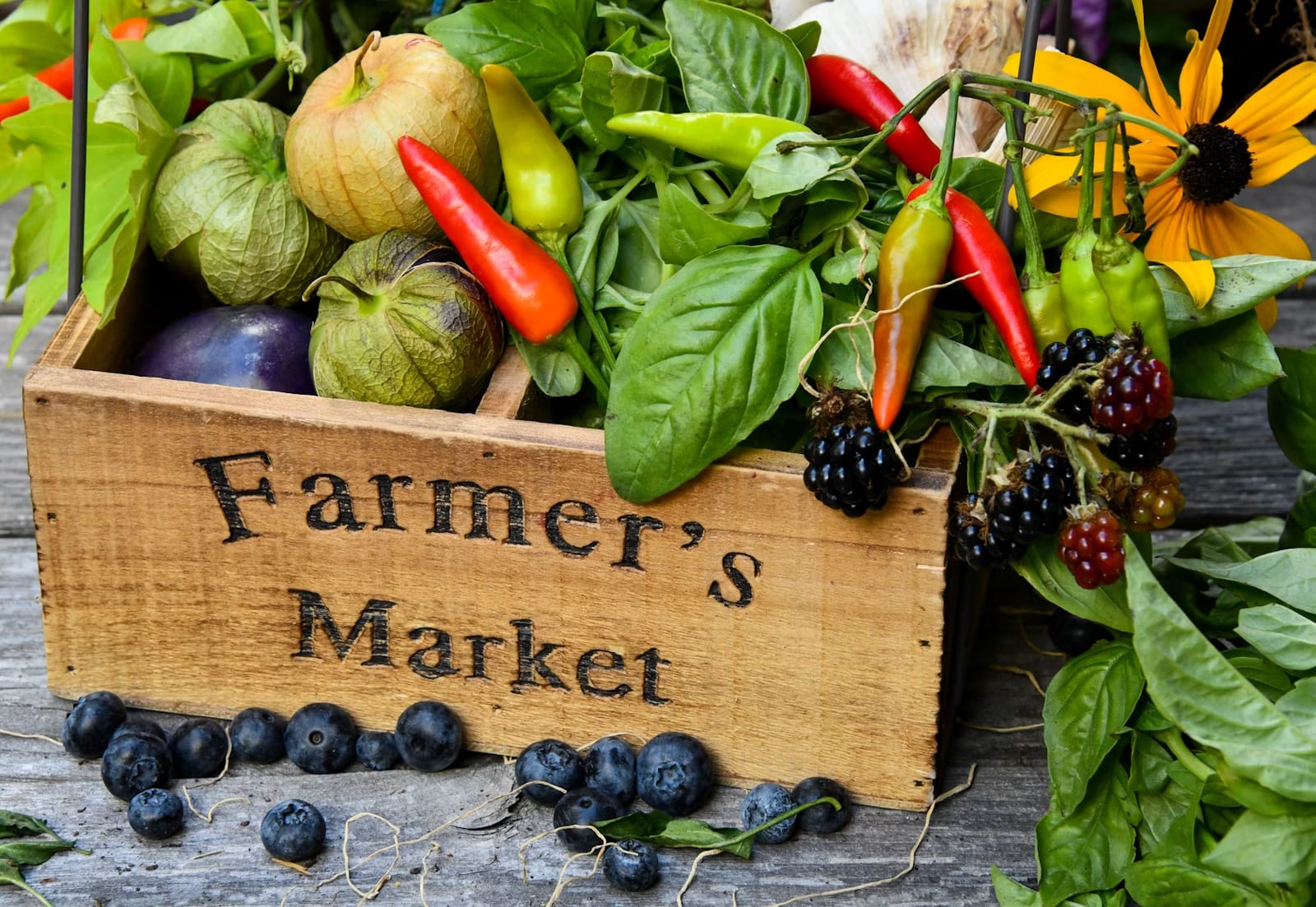 Wooden Farmer's Market box filled with peppers, tomatillos, eggplant, blackberries, basil and a sunflower